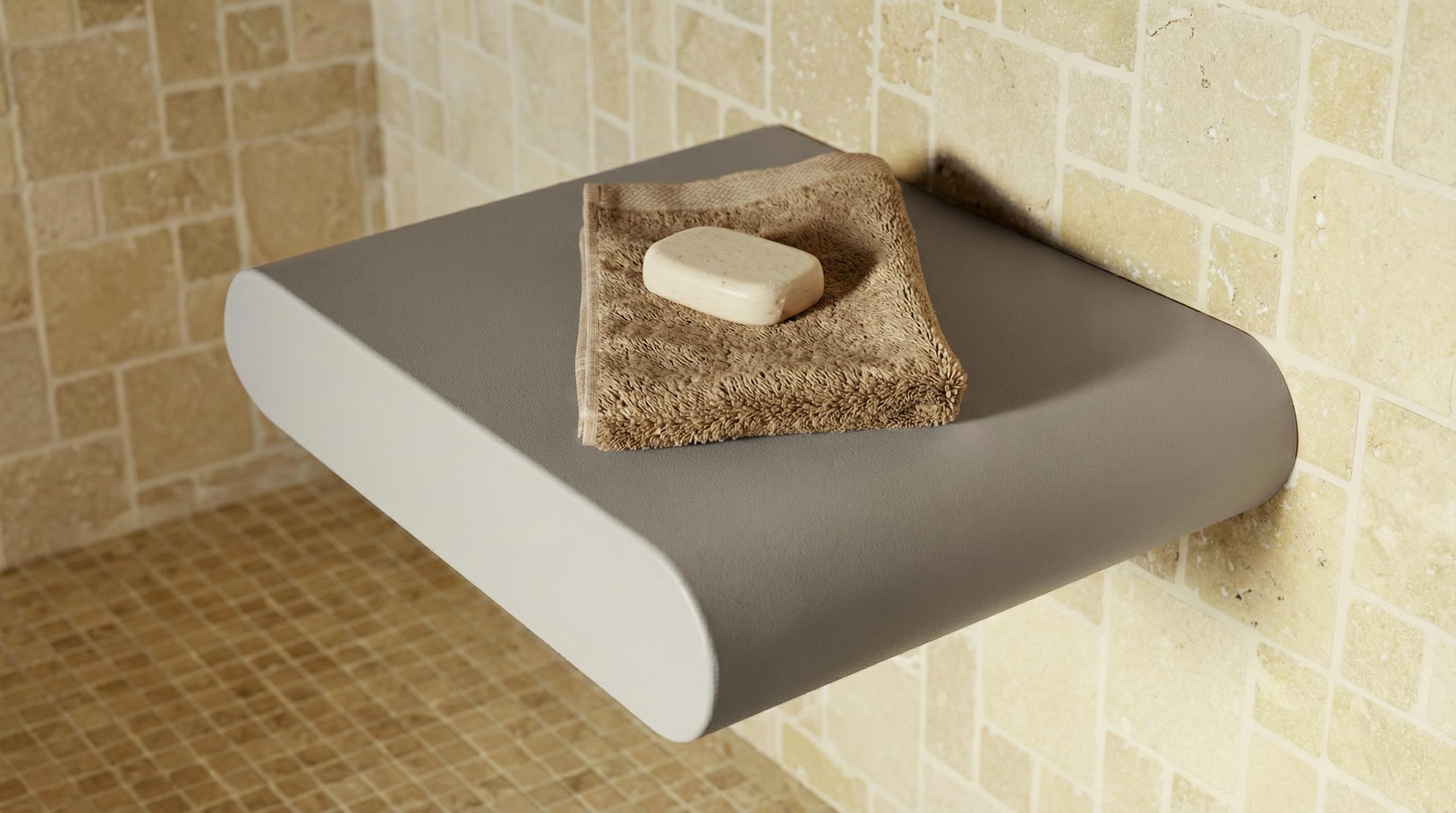 Graues, geschwungenes Duschregal an einer beigefliesten Wand, darauf ein gefaltetes braunes Handtuch und ein helles Stück Seife. Der Boden ist mit kleineren beigefarbenen Fliesen ausgelegt.